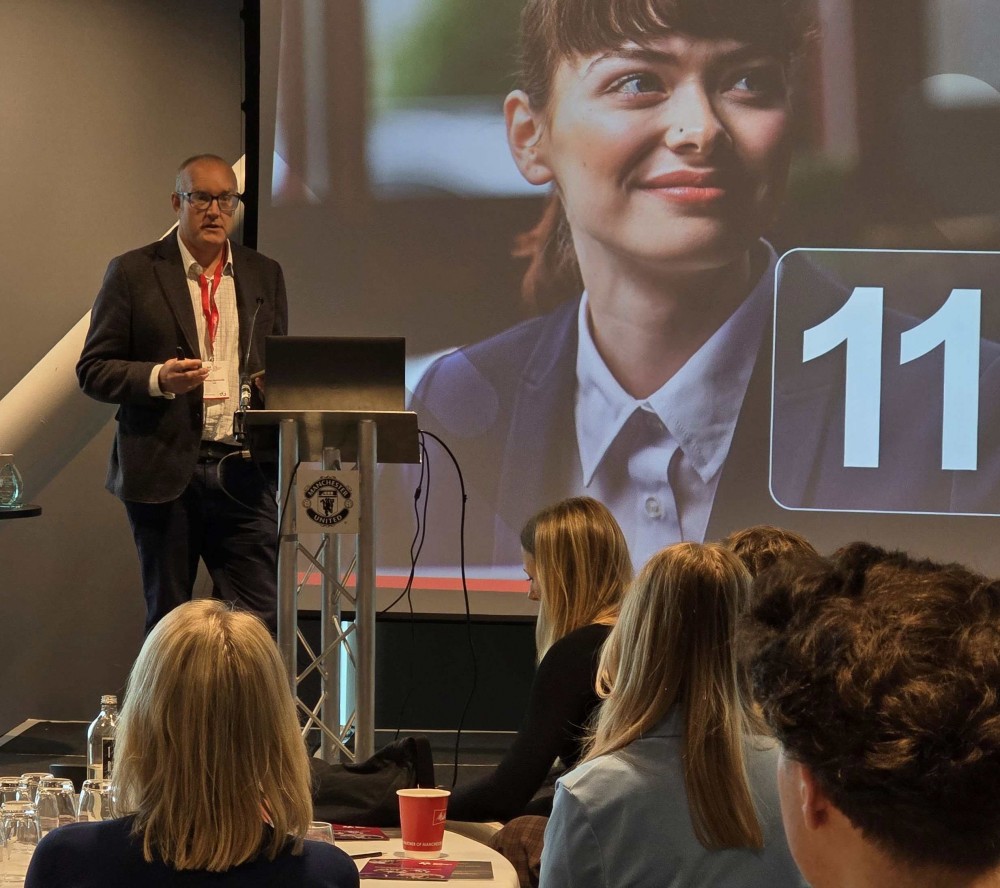 Simon Martindill on stage at SRAG Summit, with an image of a woman and the number 11, to represent 11% of women in security work in the UK.